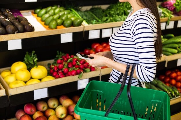 Shopping list Smiling beautiful woman stands with phone near products in store