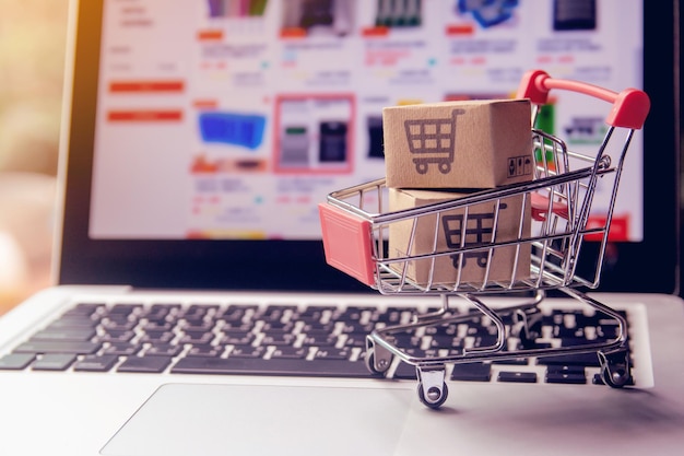 Shopping online concept parcel or paper cartons with a shopping cart logo in a trolley on a laptop