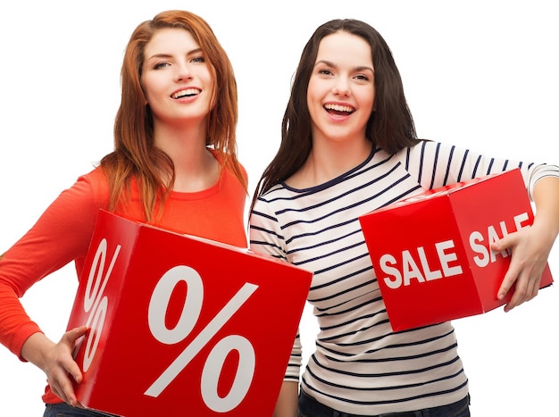 shopping, sale, and gift sconcept - two smiling teenage girls with percent and sale sign on red box