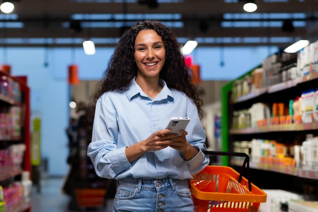 Shopping in a supermarket a young latin american woman stands between rows of shelves with a cart he