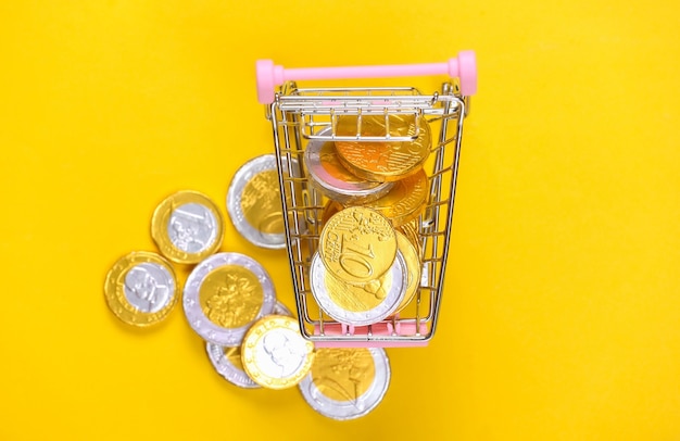 Shopping theme. Mini Supermarket trolley with coins on yellow.