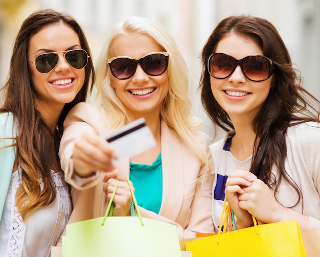 shopping and tourism concept - beautiful girls with shopping bags and credit card in ctiy