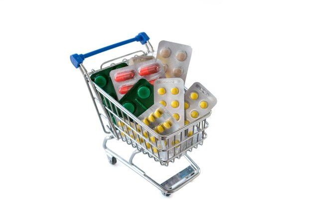 Shopping trolley with blisters of medical capsule pills on white background.