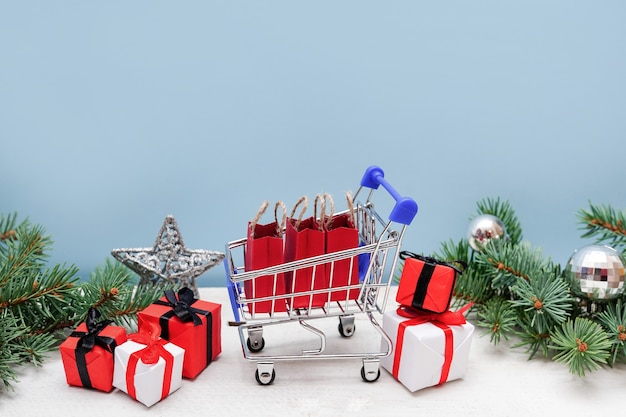 Shopping trolley with gift boxes and branches of fir-tree with decoration on blue background. Christmas and New Year sale.