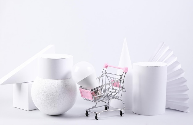 Shopping trolley with led light bulb and geometric shapes on white background Minimalism Abstract background concept art