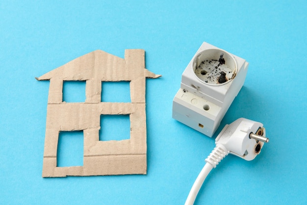 Short circuit concept of home electrical appliances Burnt plug and socket next to a cardboard house