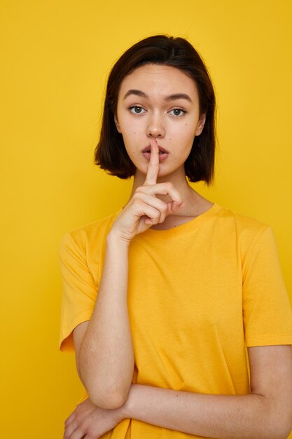 Short haired brunette yellow tshirt summer style hand gesture yellow background