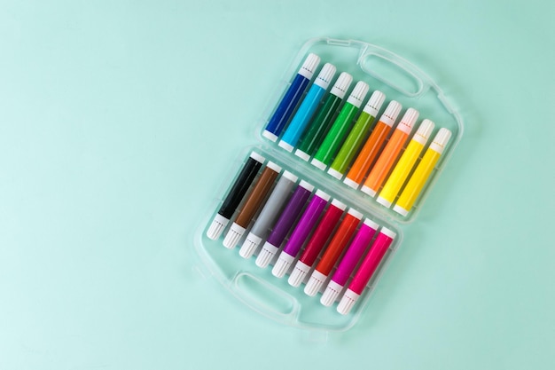 Short multicolored markers in a plastic box on a blue background