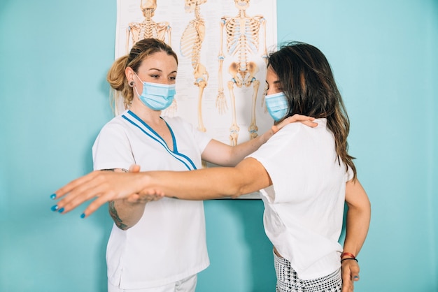 Short shot of a female Caucasian physical therapy professional in a clinic doing an observation on the arm before treating a client with a face mask due to the covid 19 coronavirus pandemic.