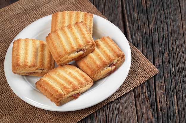 Shortbread cookies with jam in plate on wooden surface