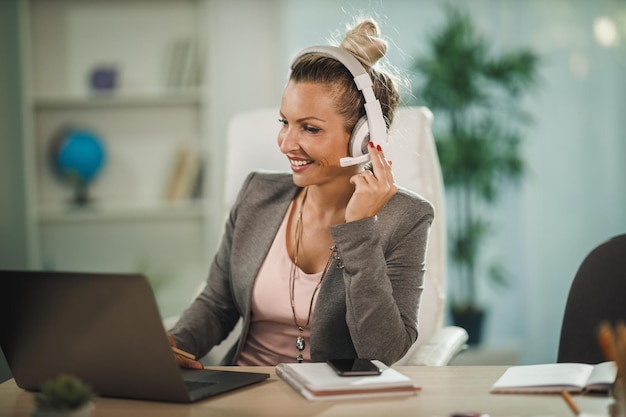 Shot of a attractive young businesswoman sitting alone in her home office with headphones and working on laptop during COVID-19 pandemic.