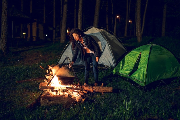 Shot of an attractive young woman cooking dinner while camping in the woods