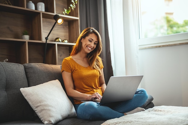 Shot of an attractive young woman sitting cross legged on the sofa and using her laptop at home.