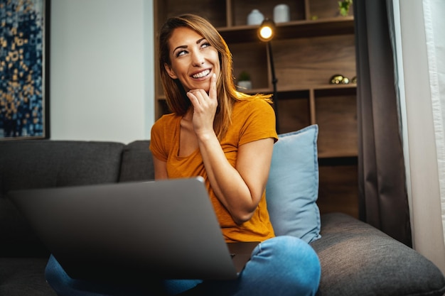 Shot of an attractive young woman sitting cross legged on the sofa and using her laptop at home.