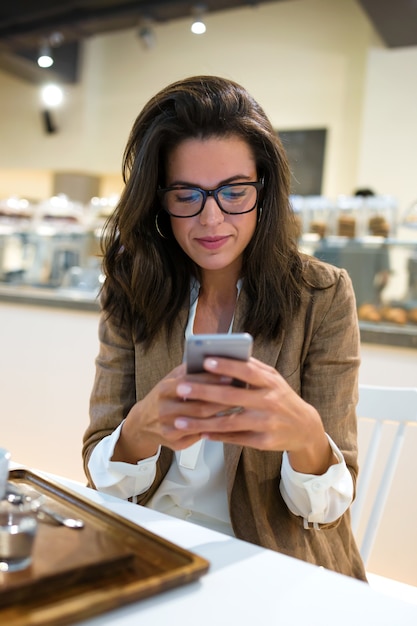 Shot of beautiful young businesswoman with eyeglasses texting with her mobile phone in the coffee shop.