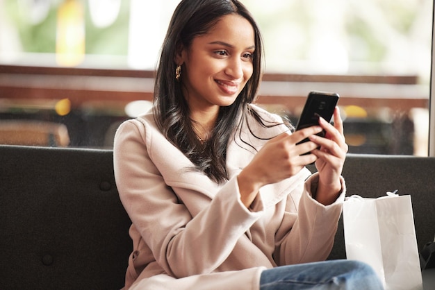 Shot of a beautiful young woman taking a break from shopping to send a text