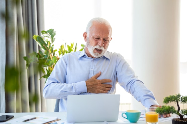 Photo shot of a businessman holding his chest in pain while seated at his desk heart attack