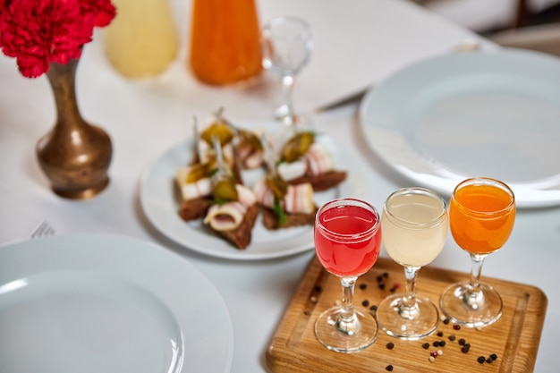 Shot of colorful alcoholic drink on a wooden stand against the served table with snacks