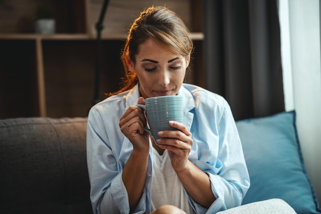 Shot of an cute young woman sitting on the sofa and enjoying a cup of coffee at home.