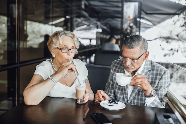 Shot of an elderly couple laughing and having a coffe together, summer terrace in modern restaurant.