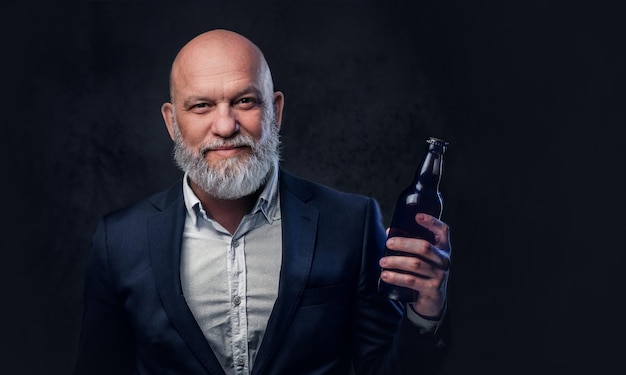 Shot of fashionable old man dressed in suit with bottle against dark background.