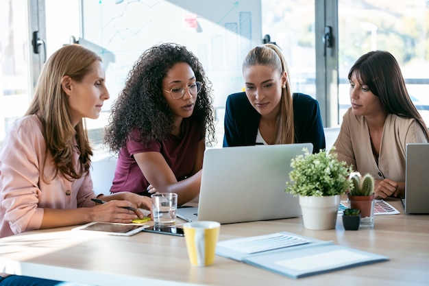 Shot of four beautiful smart business women work with laptops on the desk in the coworking space in the office.