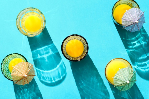 Shot from above of glasses filled with orange juice illuminated with hard light on blue background