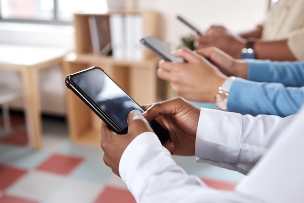 Shot of a group of unrecognisable businesspeople using their smartphones in a modern office