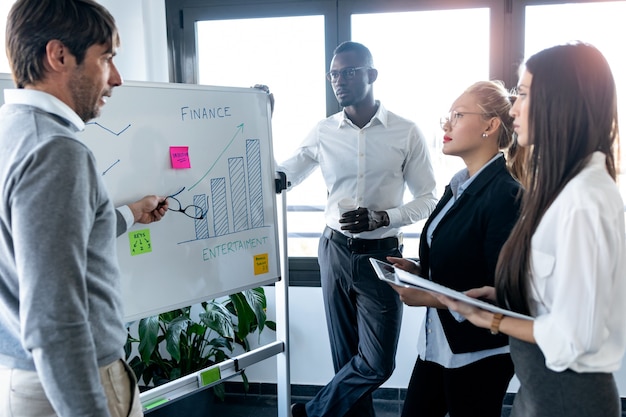 Shot of handsome businessman pointing to whiteboard while explaining to the project to his colleagues on coworking place.