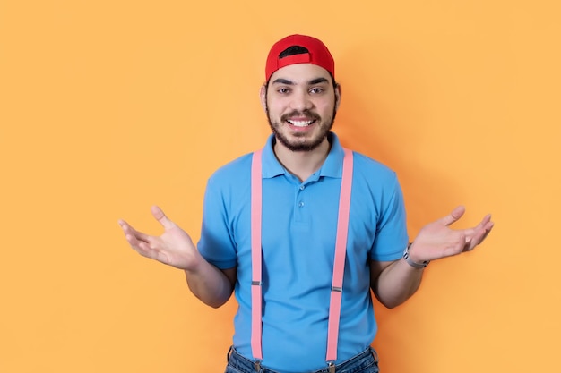 Shot of happy man with beard shrugging with opened arms over yellow background looking at camera