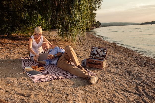 Shot of a happy senior couple looking at tablet on a picnic at the riverbank