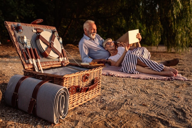 Shot of a happy senior couple looking at a tablet while having a picnic at the riverbank