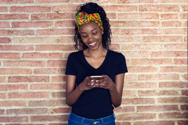 Shot of happy young woman using her mobile phone while standing in front of a wall.