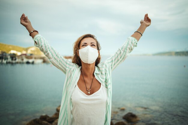 Photo shot of a happy young woman with protective n95 mask enjoying while spending time on the seaside during the covid-19.