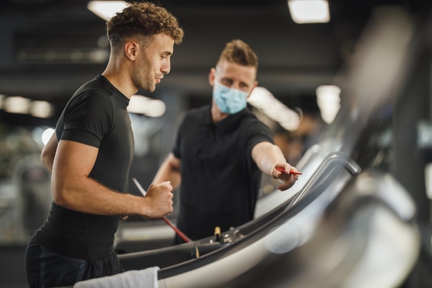 Shot of an muscular young man jogging on the treadmill at the gym. He is working out with personal trainer.