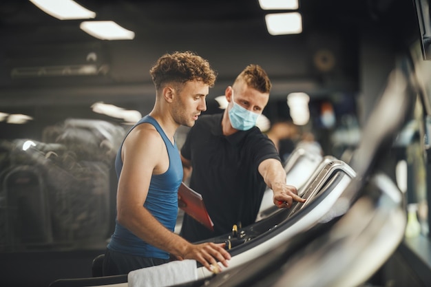 Shot of an muscular young man walking on the treadmill at the gym. He is working out with personal trainer.