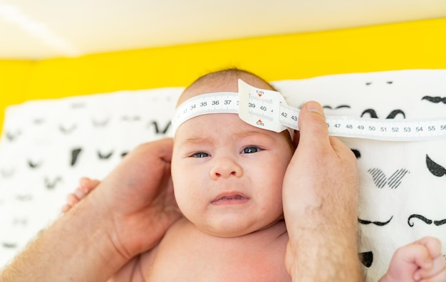 Shot of a pediatrician examining newborn baby Doctor using measurement tape checking babys head size Closeup