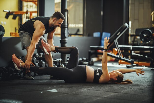 Shot of a pregnant woman doing stretching exercises with personal trainer at the gym.