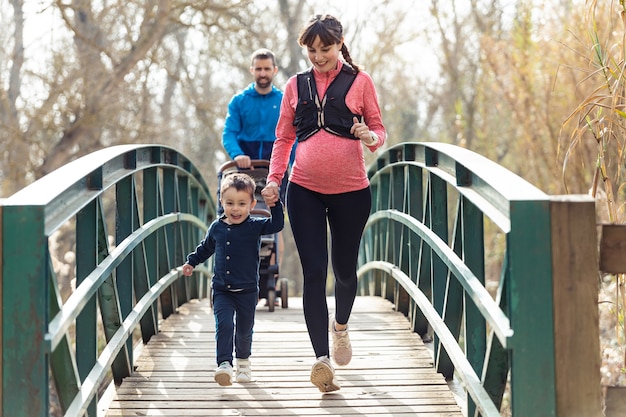 Shot of pregnant young woman with her little son running while enjoying the time together outdoor.