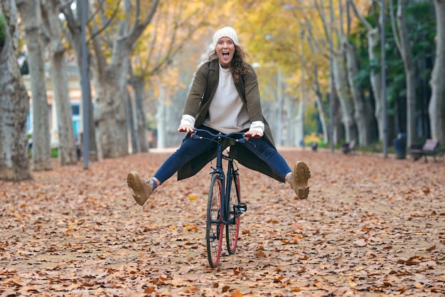 Shot of pretty funny woman with a vintage bike enjoying time while cycling through the park in autumn.