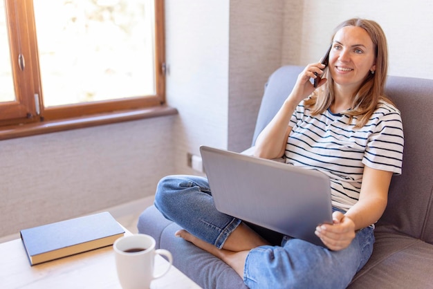 Shot of pretty young woman using her mobile phone while working with laptop