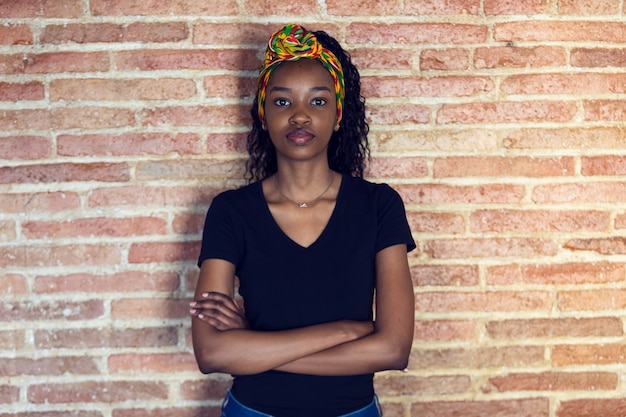 Shot of serious young woman looking at camera with arms crossed while standing in front of a wall.