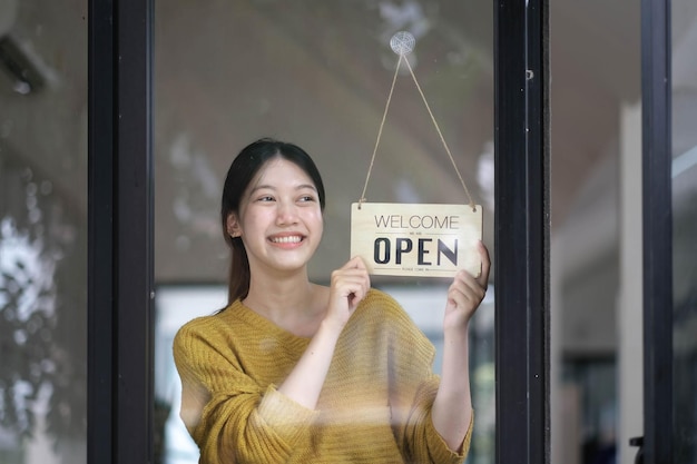 Shot of smiling Asian young sme small business owner wearing apron and standing white open singnear coffee shop door asian business woman barista cafe owner SME entrepreneur seller concept