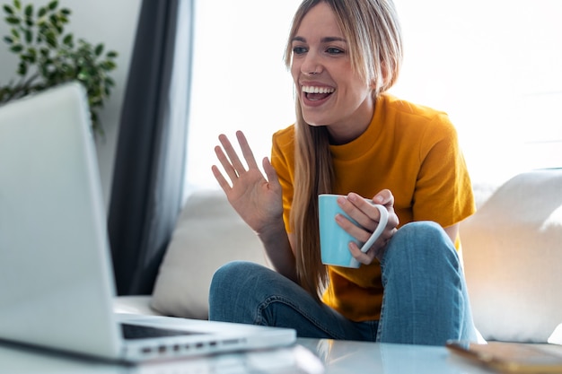 Shot of smiling young blonde woman having videocall on laptop sitting on the couch