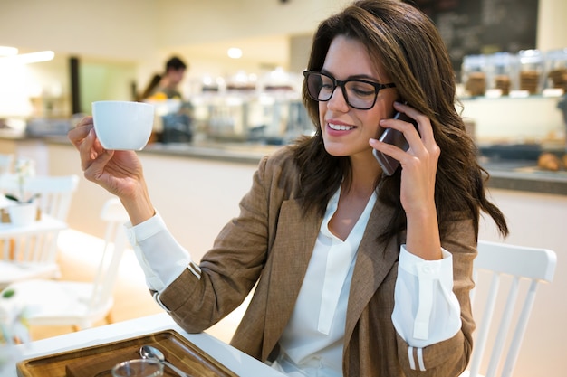 Shot of smiling young businesswoman talking with her mobile phone in the coffee shop.