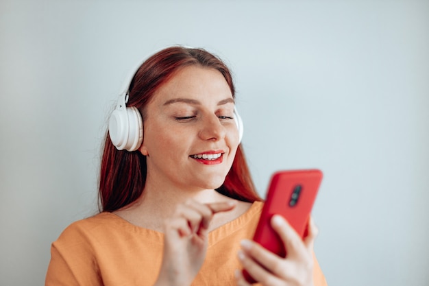 Shot of smiling young woman wearing wireless white headphones using her mobile phone enjoying stylish modern music melody