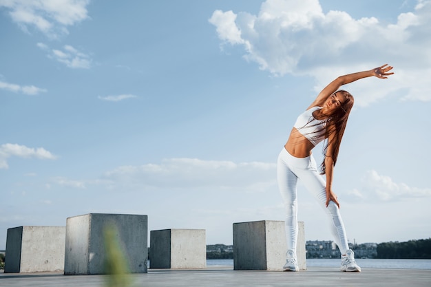 Shot of sportive woman doing fitness exercises near the lake at daytime