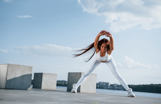 Shot of sportive woman doing fitness exercises near the lake at daytime