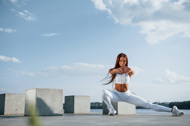 Shot of sportive woman doing fitness near the lake at daytime