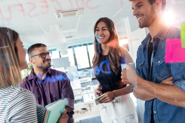 Shot of successful business team discussing together in front of office glass board in the coworking space.